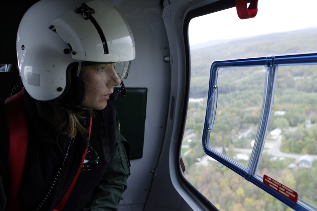 A woman wearing a helmet looks out the window of a Lifeflight helicopter.