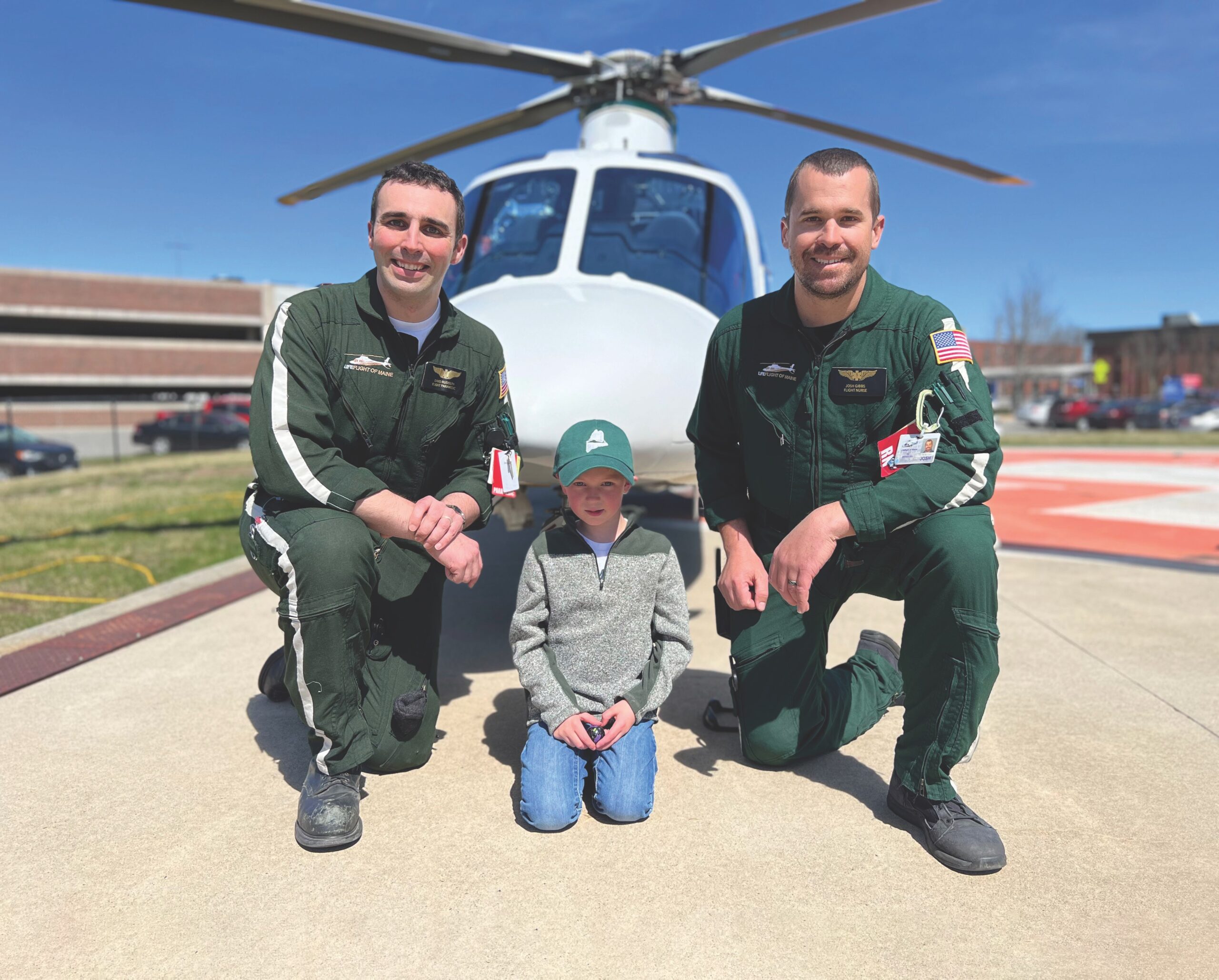 Two male LifeFlight staff and a small boy pose in front of a helicopter