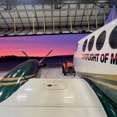 View of a pink and purple sunset from an open hangar, over the wing and fuselage of LifeFlight airplane.