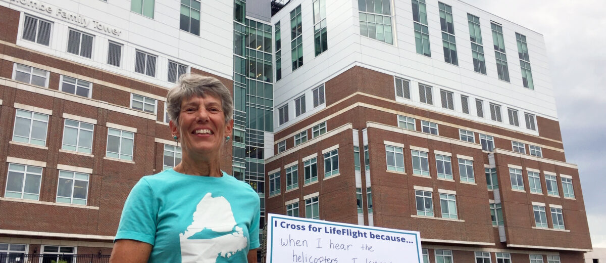 Sue Cook holding a sign reading. "I cross for LifeFlight because...when I hear the helicopters, I know someone is getting the critical care they need."